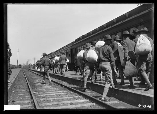 Leaving camp, at station, train on track to right, men with bags