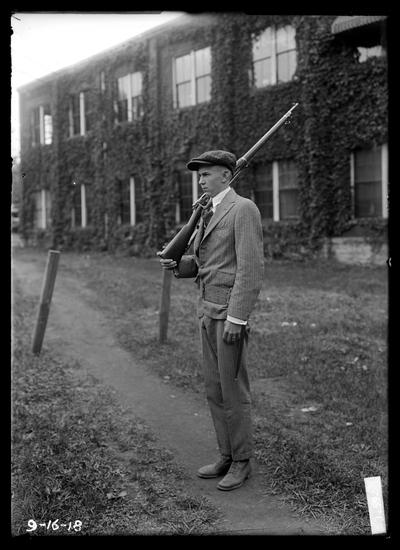 Walking the post-boy in civies with rifle on shoulder, ivy covered building Mechanical Hall