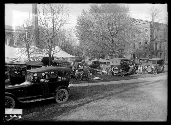 Auto shop in tent, surrounded by cars, Administration Building (Main Building) in background, Miller Hall to right