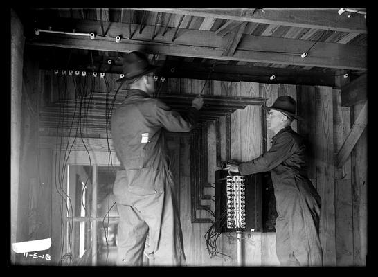 Electricians wiring building, fuse box, two men working, wooden building