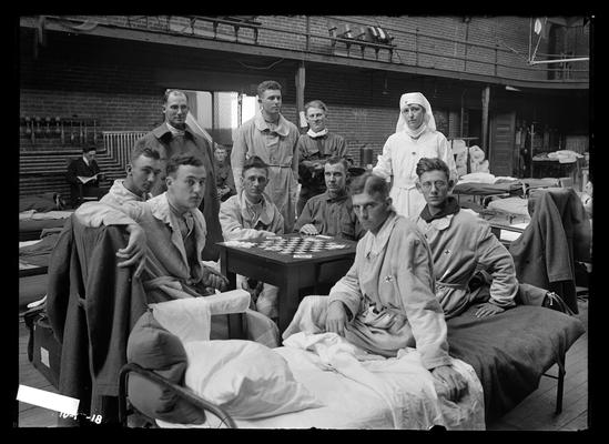 Recuperating (from flu?), some at card table, two with robes bearing cross on side of cot, nurse