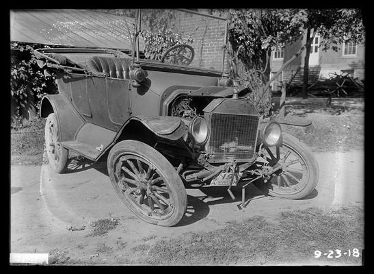 Ford which has been wrecked, United States of America Technical Training, University of Kentucky on license plate, house in right background