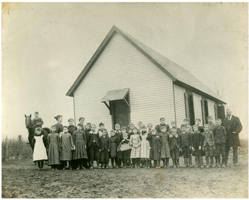 Group portrait of Donerail students standing in front of school with teacher Emma Latham and M.A. Cassidy, Superintendent of Fayette County Public Schools until 1903. Handwritten on verso of 14b, During Mr. M.A. Cassidy's administration. (Two copies)
