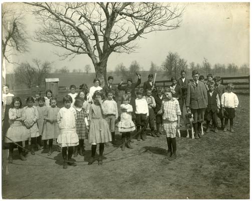 Group portrait of Elmendorf students, with teacher Ella Ford, standing in front of school located off Paris Pike. Handwriting on verso. (Four copies)