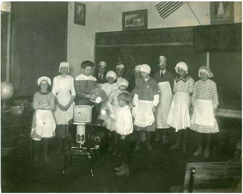 Kitchen workers and Ella Ford serve soup to a student. Handwritten on verso, Mrs. Ella Ford and school at lunch