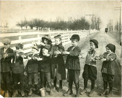 Group portrait of Greendale students posed with their hands outstretched. There is a horse and buggy in the background. Handwriting on verso. (Three copies)