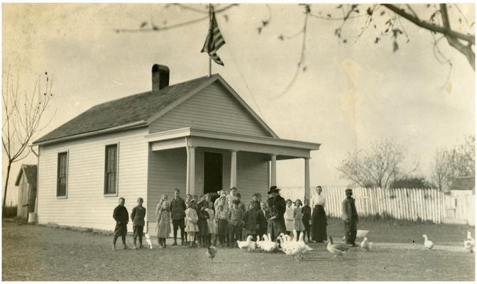 Group portrait of Lisle students standing in front of the school house with Nannie Faulconer (1865?-1940) and their teacher, Lizzie Barkley. Handwriting on verso. (Four copies)