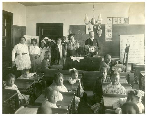 Group portrait of Maddoxtown students sitting at their desks with State School Supervisor F.C. Button, Nannie Faulconer (1865-1940), and Mattie Dalton. Handwritten on verso, Maddoxtown-Mrs. Nannie G. Faulconer, Supt. Schools of Fayette County. Dr. F.C. Button, State School Supervisor. Miss Mattie Dalton--afterwards School Supt. (Three copies)