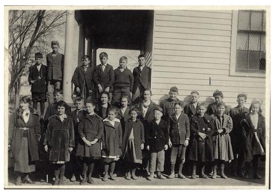 Group portrait of New Brighton students and teacher Millie Mae Watson standing in front of the school house. Handwritten on verso, New Brighton. Miss Millie Mae Watson Prin