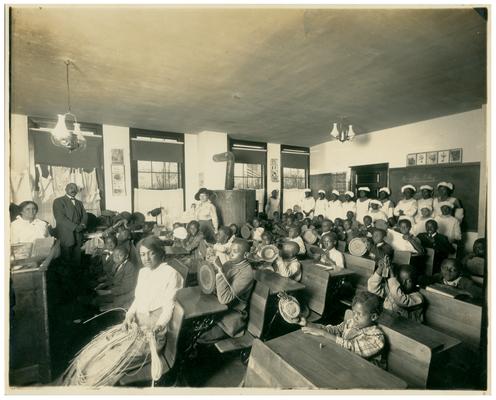 Group portrait of students sitting at their desks with Nannie Faulconer (1865?-1940) in the background