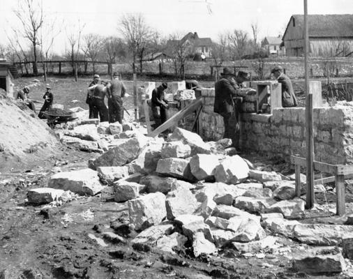 Project #2365 District 2: Construction of a municipal building, housing the city hall, fire station, and city jail in the City of Monticello, KY. The building is being constructed of native stone, quarried as part of the project. The view shows workmen laying the stone walls. Photographed March 25, 1936