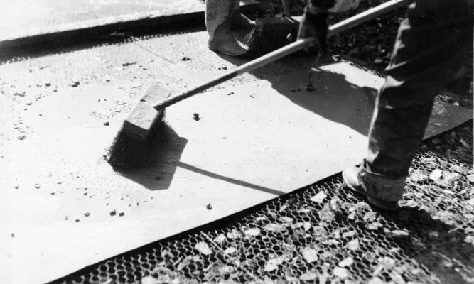 Project #1201 District 6: Utilizing old brick in reconstructed city streets. Close-up of man brushing the cement grout off the piece of sheet metal onto the crushed brick. Photographed February 27, 1936