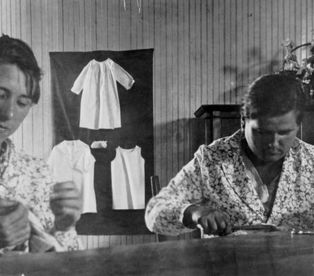 Project #1665 District 3: The Sewing Projects for Women. Two women of the Oldham County Training Work Center at LaGrange shown making garments. Children's clothing made on this project is displayed on the wall