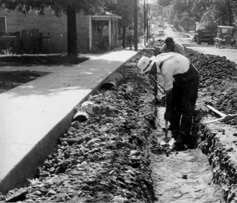 Project #1935 District 6: The widening and resurfacing with rock asphalt of Clay and Washington streets in the City of Shelbyville, KY, and the reconstruction of 21,000 feet of curb and gutter are provided by project #1935. View shows workmen widening street. Photographed June 4, 1936