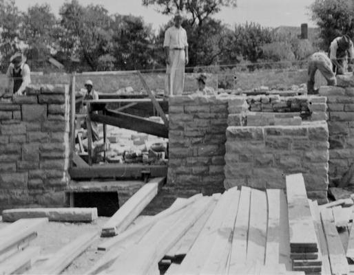 Project #1303 District 4: Gymnasium Building, Sharpsburg, KY. Construction of a combination gymnasium-auditorium building, of native limestone for the Sharpsburg Independent School in Bath County. The photograph, taken July 22, 1936, is an exterior view, showing stone masons laying wall
