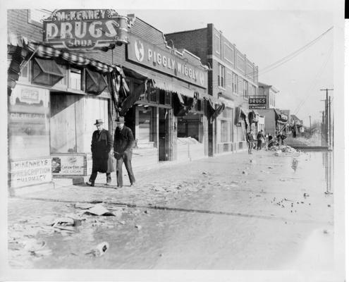 Men walking past McKenney Drugs and Piggly Wiggly stores on flood damaged street in Louisville, KY