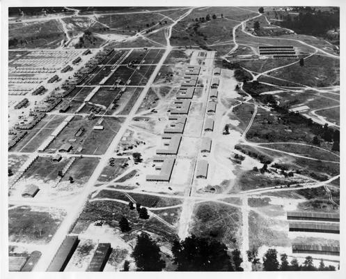 Aerial view (oblique) of seven mess halls and seven latrines, which comprise a portion of the National Guard training headquarters at Ft. Knox directed by the WPA. In the upper left corner of this view may be seen concrete tent floors erected by the WPA. In the upper and lower right hand corners may be seen motor sheds erected by the WPA