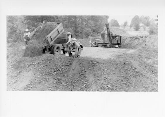 Project #2187, Master Project #2808 District 6: Project #2187 of Master Project #2808 is the grading and draining of the Shepherdsville Road in Hardin County. View shows heavy grading work in progress with use of a small revolving gas shovel and dump trucks. Photograph taken October 7, 1936