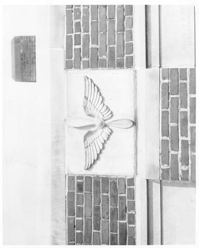 Unidentified plaque on a brick wall; the plaque consists of a pair of wings and a propeller