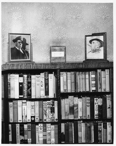 Bookshelf, lined with books and with two portraits on top of the cabinet