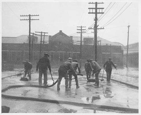 Men scrubbing a street with fire hose and brushes