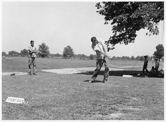 Man driving a golf ball while others watch. One of the men is Edwin J. Paxton