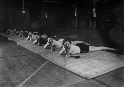 Women lying on mats on the floor of Alumni Gym pointing rifles at practice