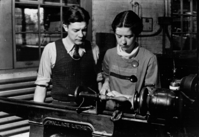 Woman using a lathe as instructor watches