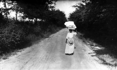 Unidentified  African-American woman on a dirt road carrying linens on her head