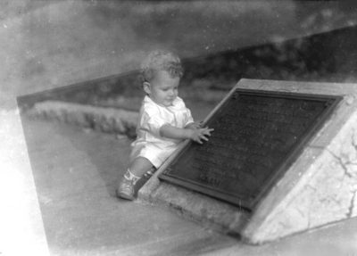 Child (Knapp family) next to a plaque for Memorial Railroad track, located next to Anderson Hall