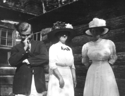 Unidentified man with two unidentified women by log cabin