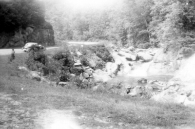 Unidentified woman in distance on left looking at creek with waterfall