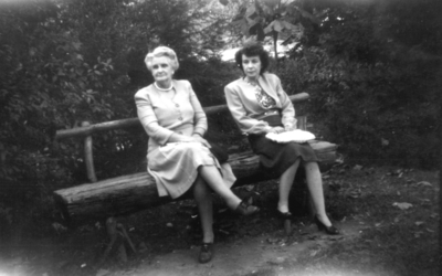 Two unidentified women sitting on bench made from a log