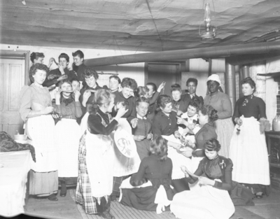 a large group of women of varying ages wearing aprons and sitting together, possibly at a candy pull