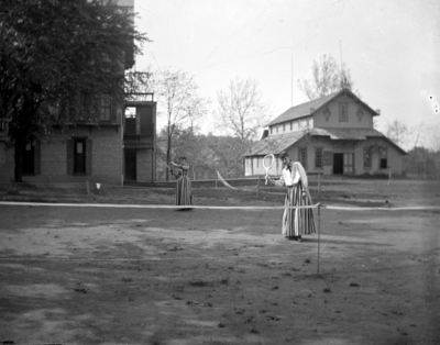 2 women outside playing tennis, possibly behind Patterson Hall on land that is now occupied by Blazer Hall