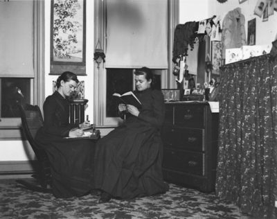 2 women sitting together inside, possibly a dorm room in Patterson Hall (built in 1904) the first women's dormitory