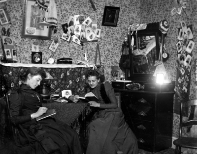 2 women sitting at a table, possibly in a dorm room in Patterson Hall,  reading and writing