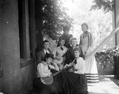 7 women sitting on a porch, 2 are holding banjos
