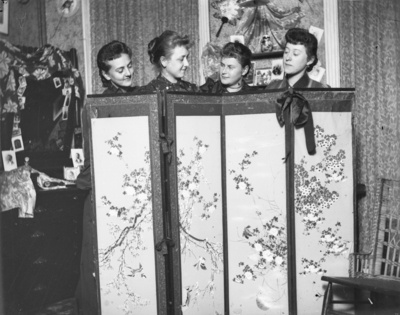 4 women standing behind a decorative screen