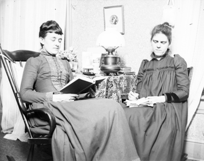 2 women sitting in chairs, one is reading a book