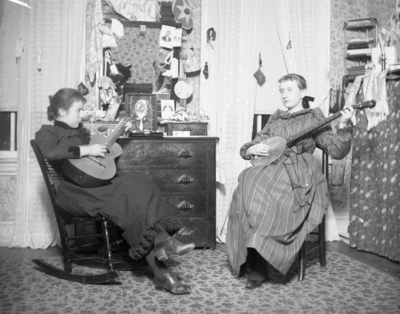 2 women playing instruments, one is playing a guitar while the other is playing a banjo