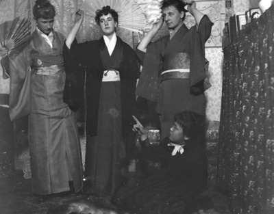 3 women dressed in kimonos with 1 woman sitting on the floor looking up at them