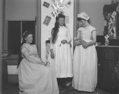 3 women who appear to be dressed in costume, 1 of them is holding a doll