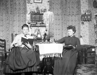 2 women, one is reading and the other is working at a table