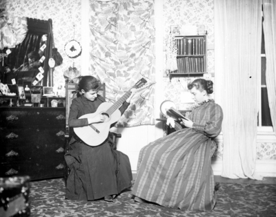 2 women, 1 is playing guitar and the other is reading