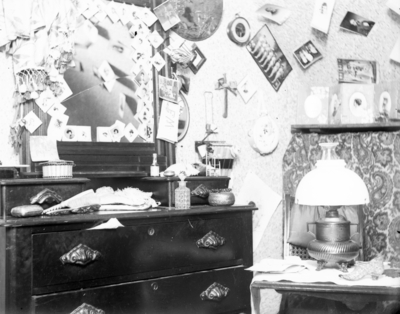 interior of a room, possibly a dorm room, a dresser and small table with a lamp on it
