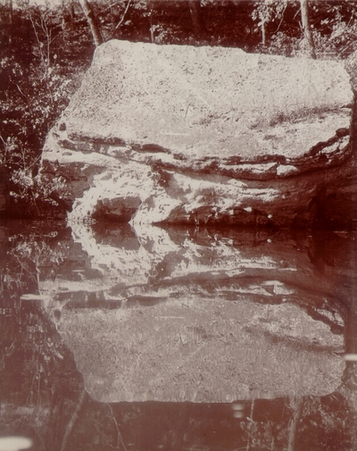 Large rock mirrored in still water pond