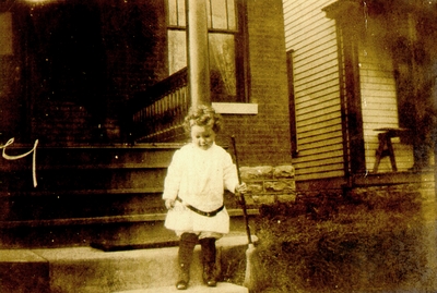 Little girl on front porch steps with broom