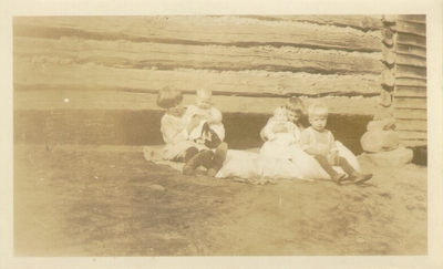 Five children sitting near log building