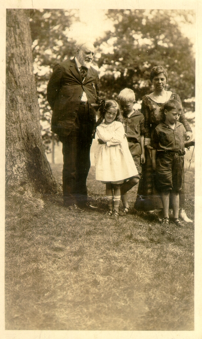 Old man, woman, and three children standing near tree